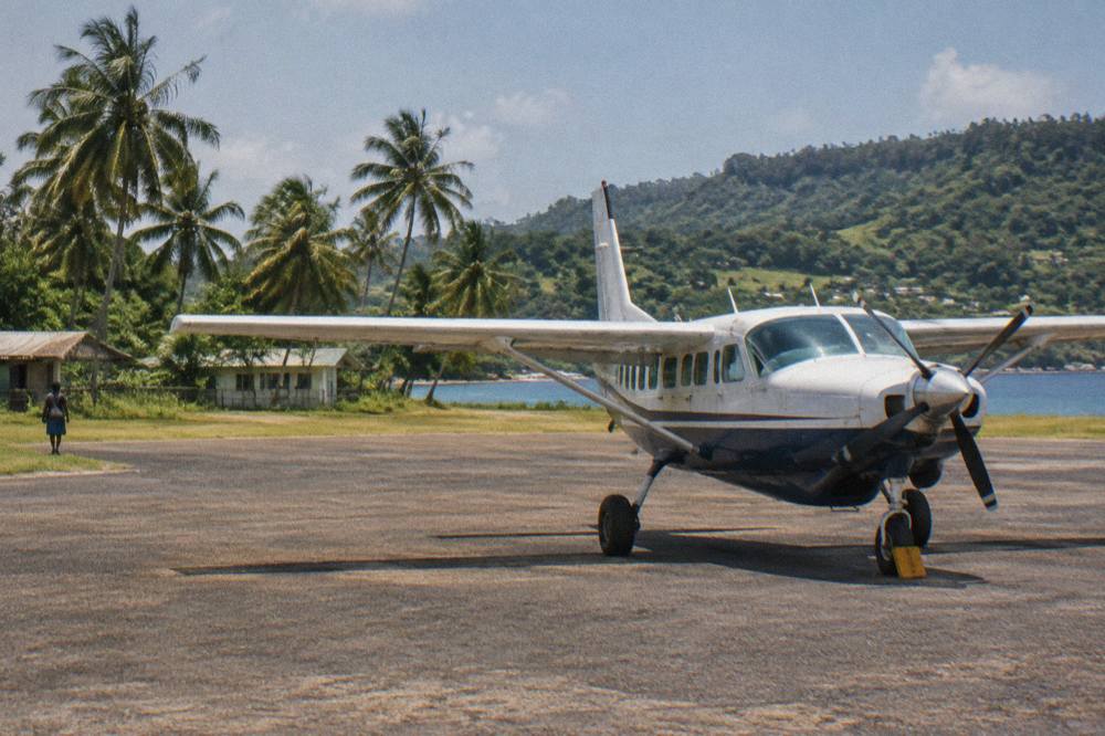 A small aircraft parked on a tropical island airstrip surrounded by palm trees