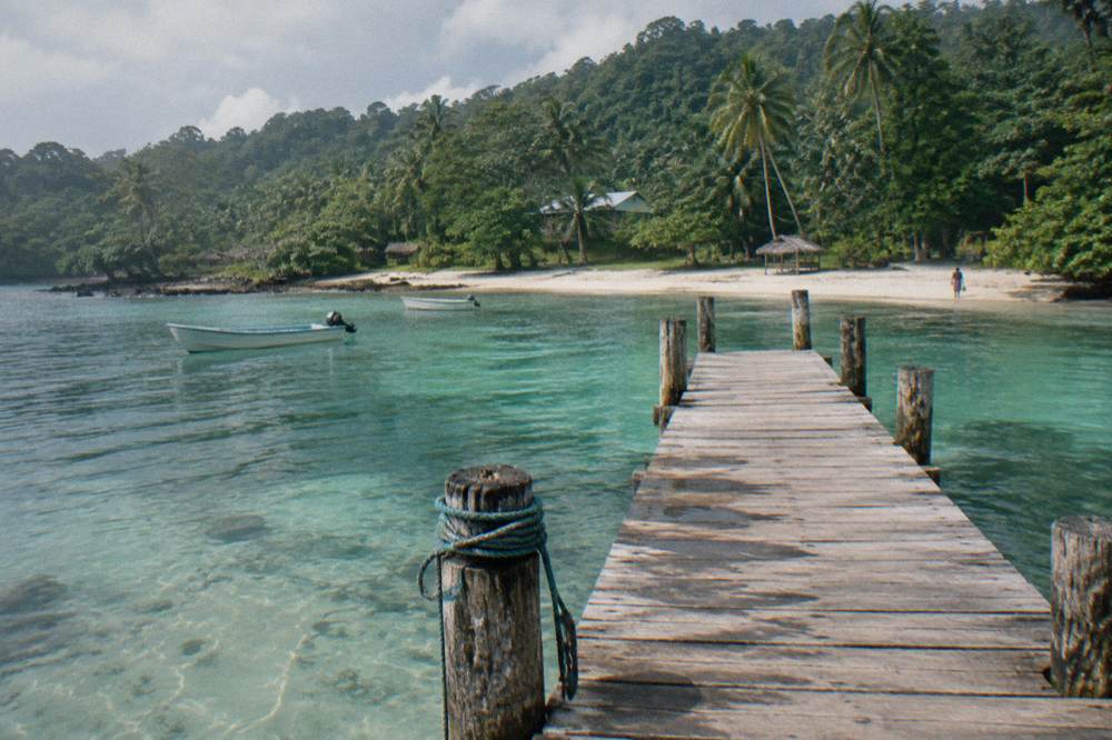 A turquoise lagoon ringed by dense green jungle with a wooden jetty extending into the water