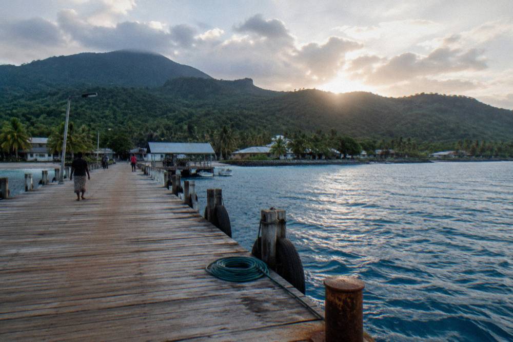 A wooden jetty extending over deep blue water toward green hills