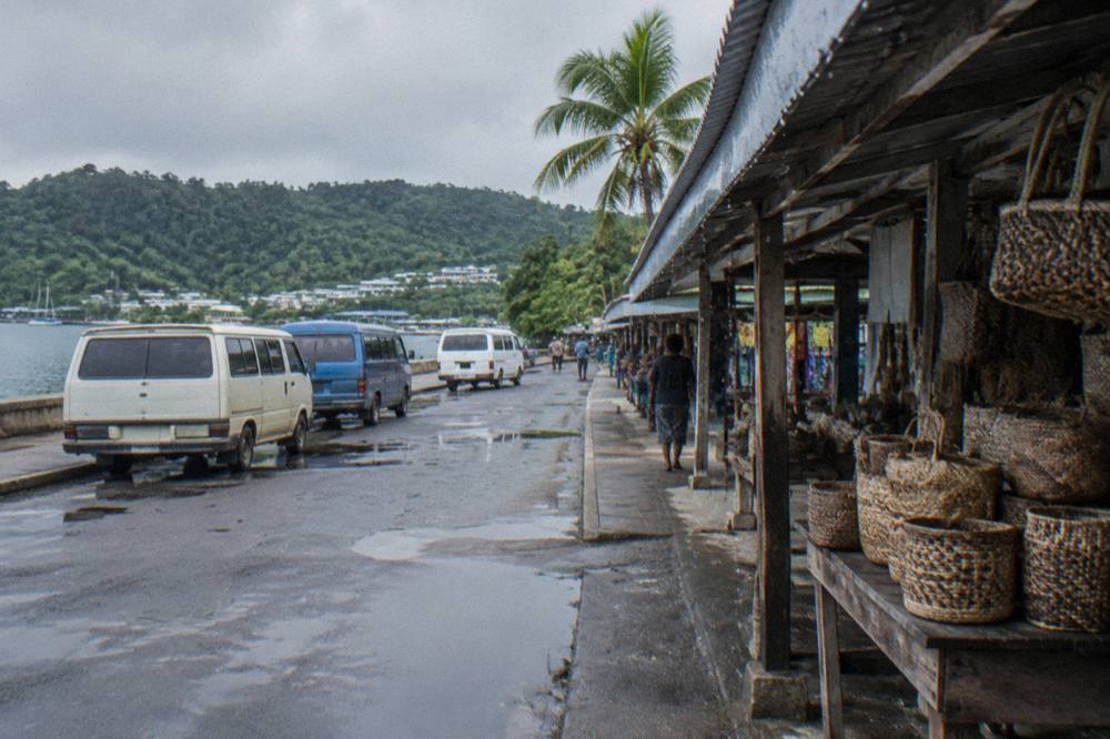 Parked minibuses and a covered market stall on a Port Vila street