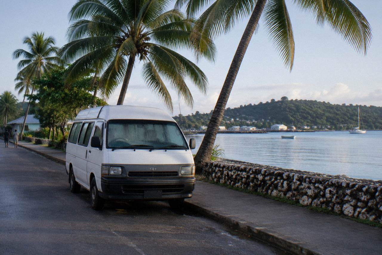 A taxi minibus parked on a seafront road in Port Vila with palm trees along the waterfront
