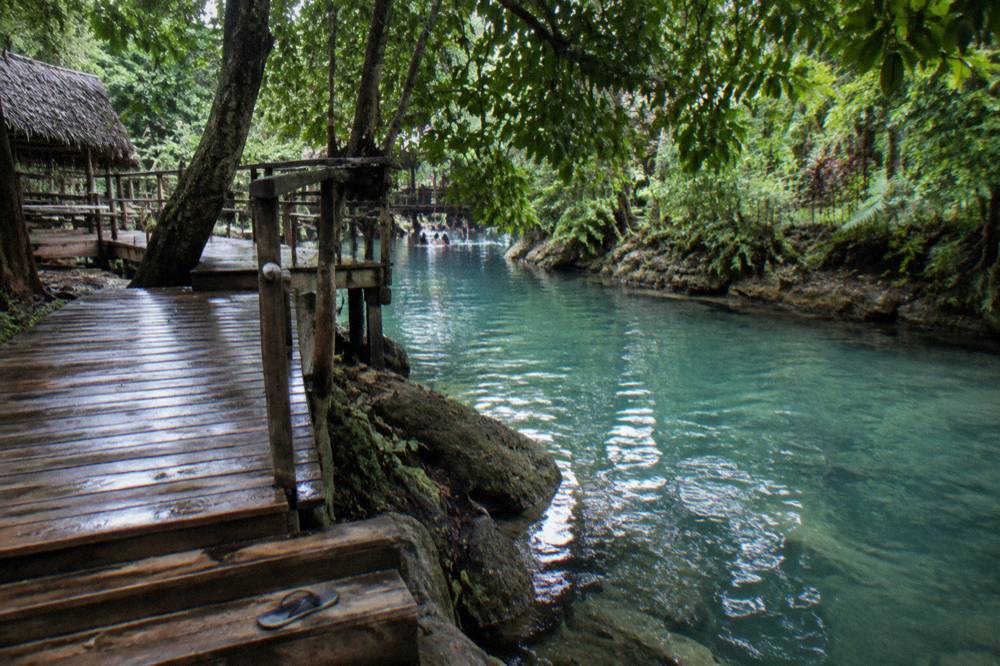 Shaded freshwater river swimming hole with overhanging trees and a wooden walking path
