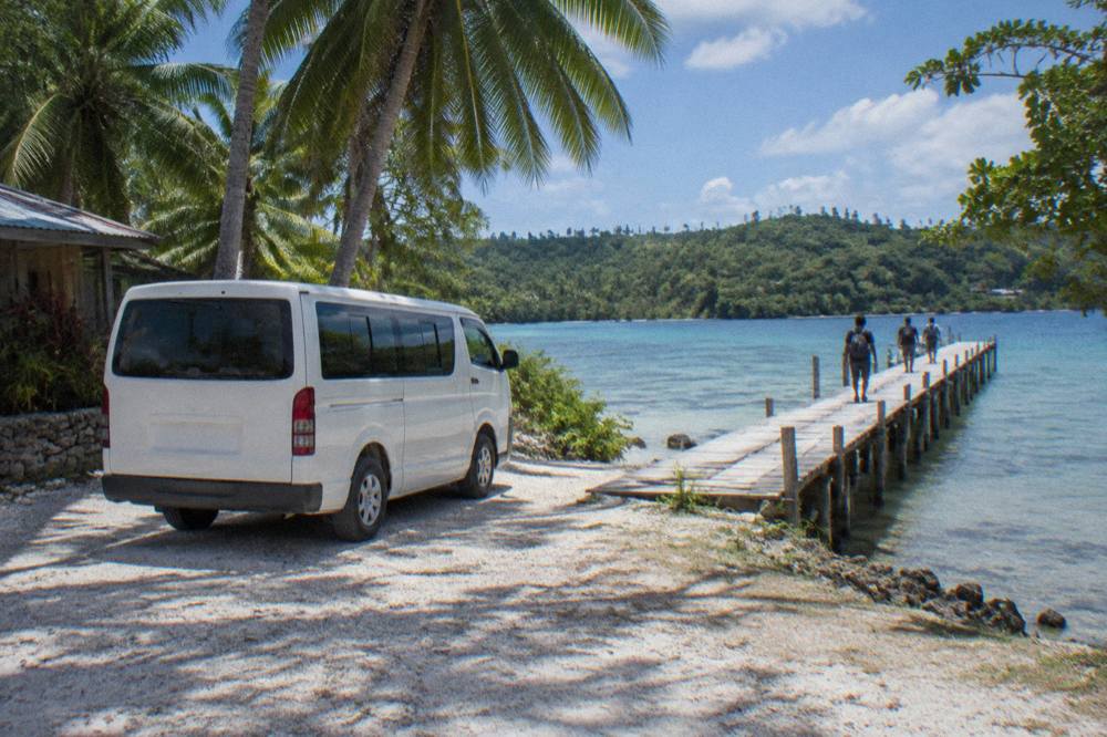 Tour van parked beside a palm-fringed lagoon with wooden jetty and clear shallow water
