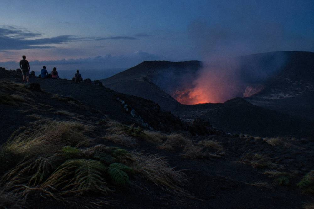 Volcano crater at dusk with a low glow above dark ash slopes