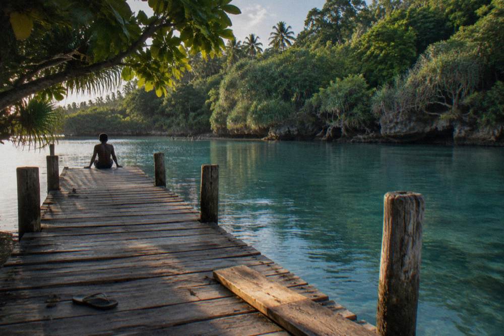 Clear blue lagoon surrounded by jungle and a wooden jetty