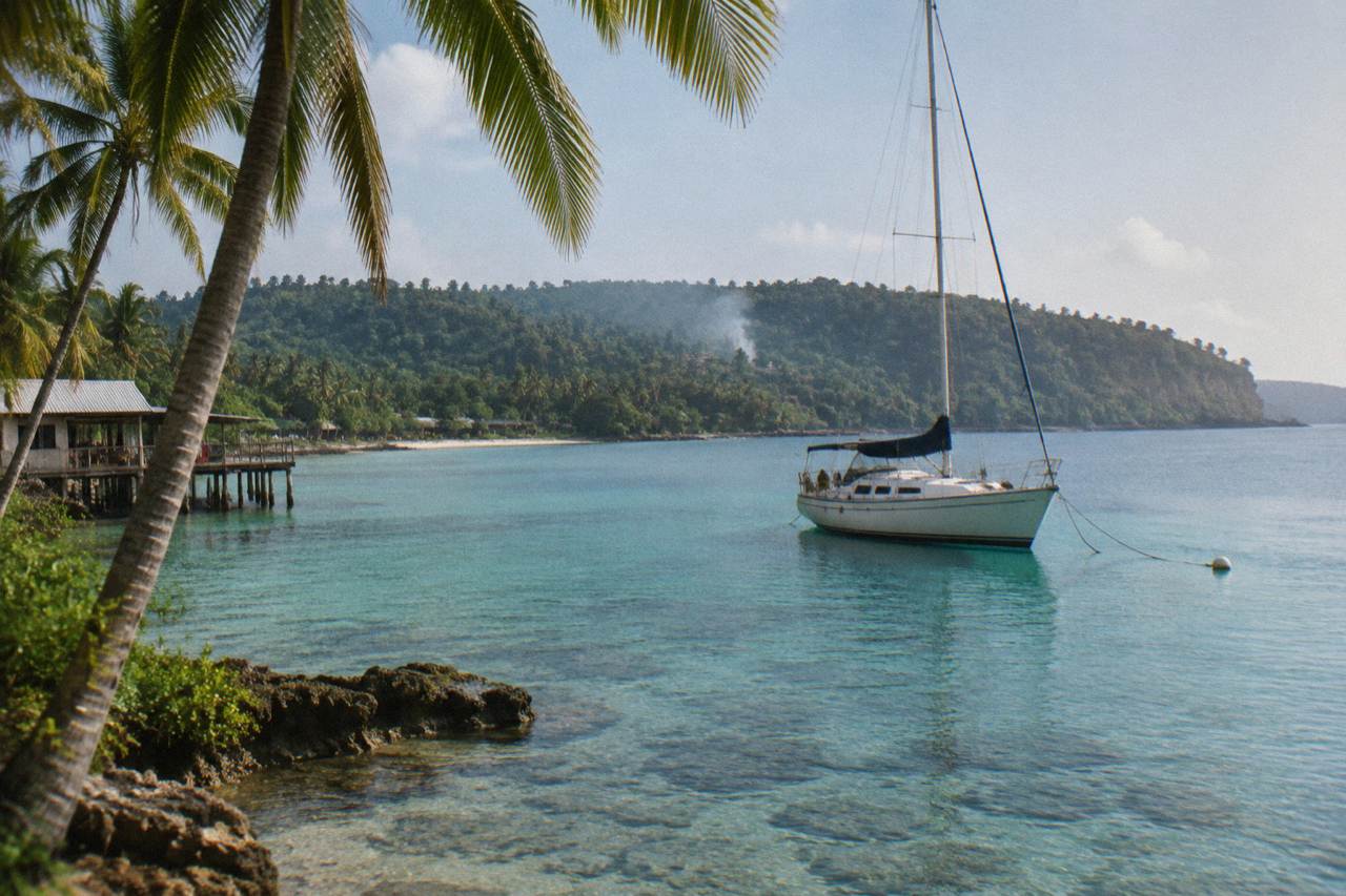 Calm turquoise bay with palm trees and a moored sailing boat near Port Vila