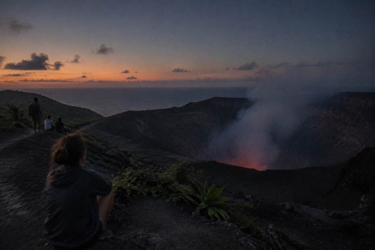 A wide volcanic crater glowing at dusk with a low plume of smoke above dark slopes