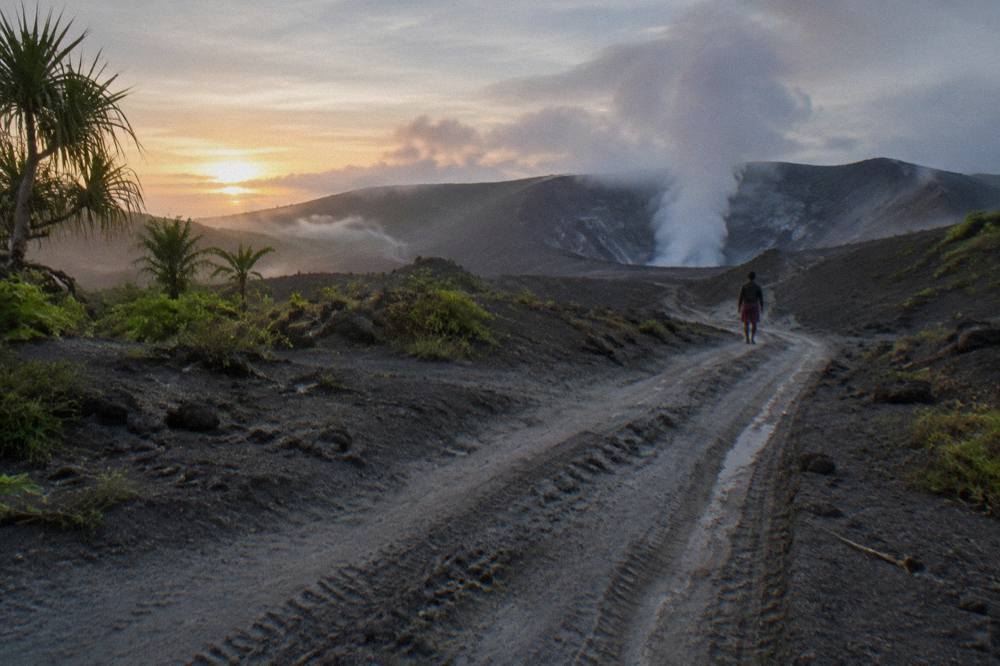 Rough 4WD track climbing through ash plain toward the glowing crater of Mount Yasur volcano