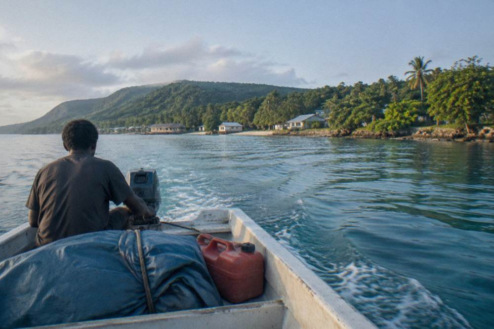 Small boat crossing clear harbour water towards a green island shoreline