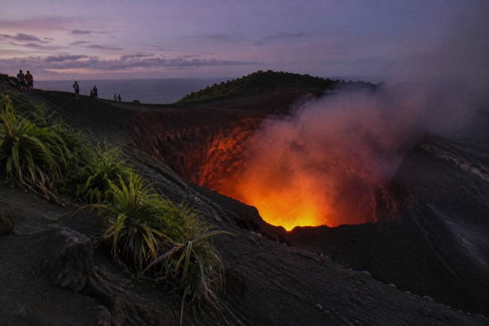 Glowing crater of Mount Yasur volcano seen from the rim at dusk with smoke drifting sideways