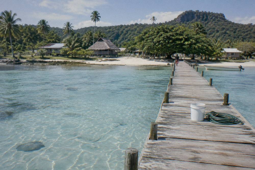 A wooden jetty extending over pale blue shallow water above a sandy seabed