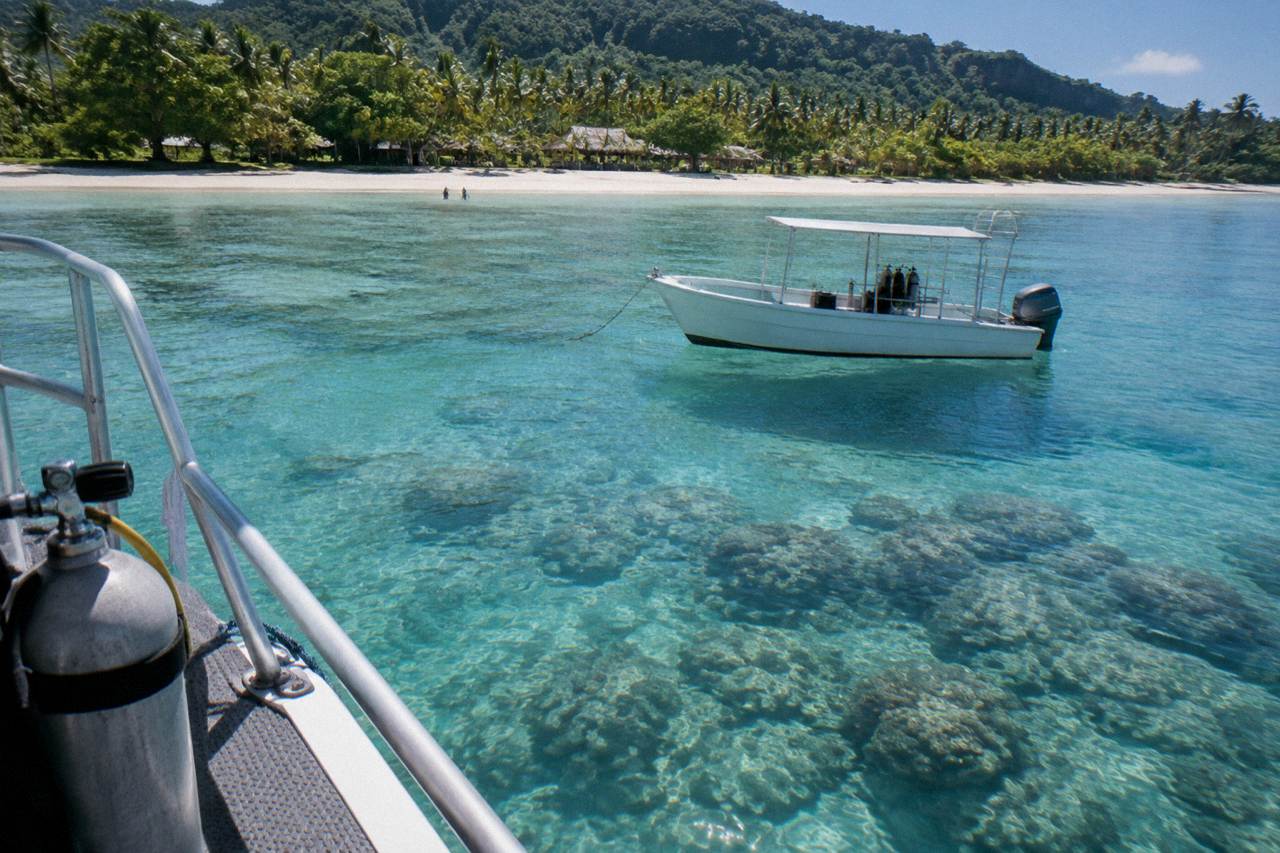 Clear turquoise water over a coral reef with a small dive boat anchored nearby