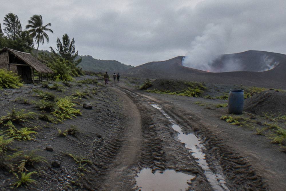 A four wheel drive track crossing grey volcanic ash plains toward a smoking crater