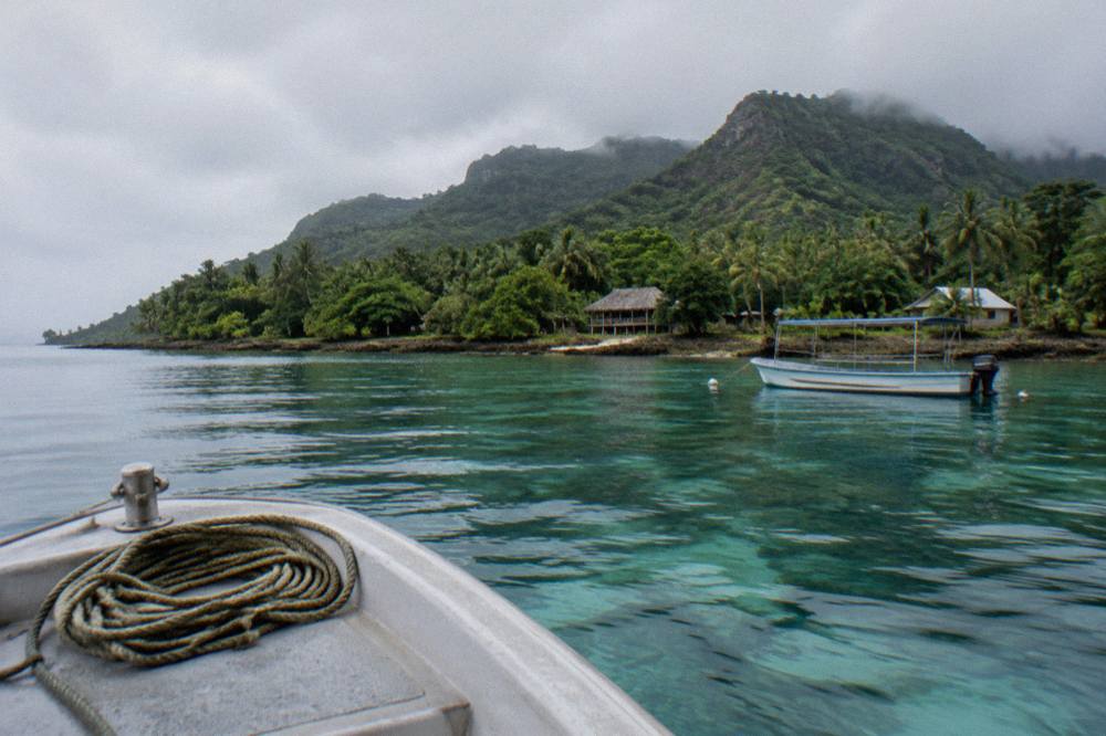 A tour boat anchored over clear shallow water near a wooded Vanuatu island