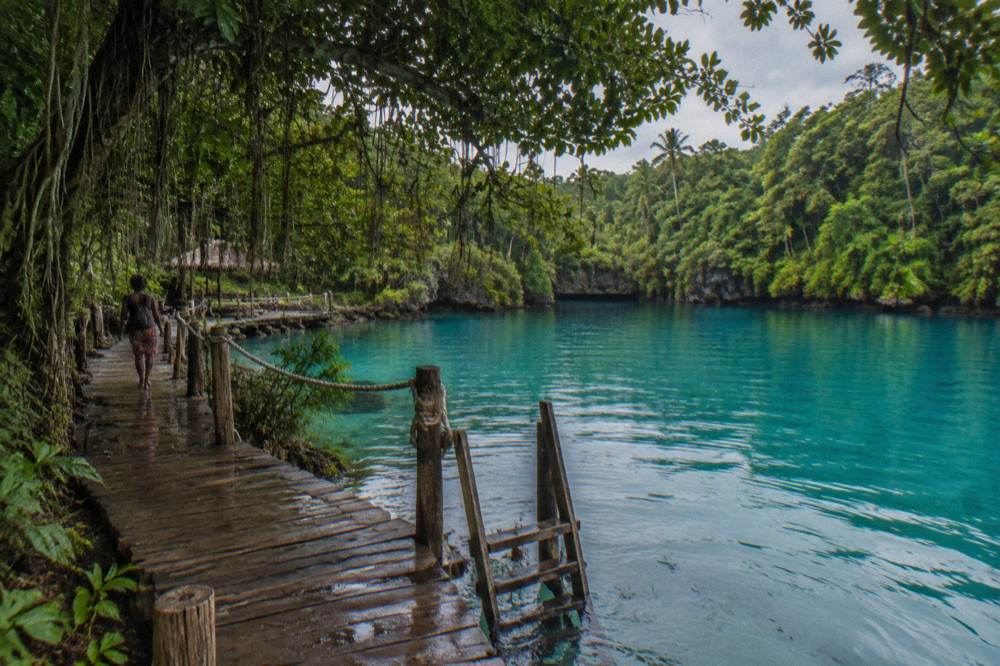 A turquoise lagoon ringed by jungle with a wooden jetty leading into clear water