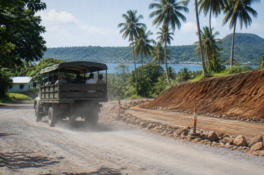 Open-air tour vehicle travelling along the palm-lined Efate ring road with green hills in the distance
