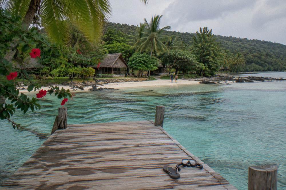 Shallow turquoise lagoon water with a wooden jetty and overhanging trees along the edge