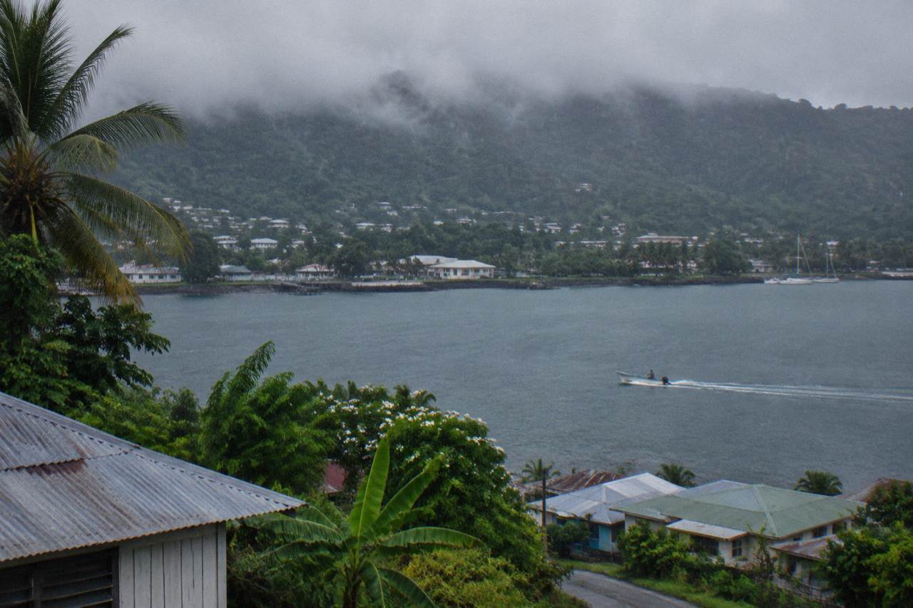 Rain clouds passing over green hills above a calm harbour town