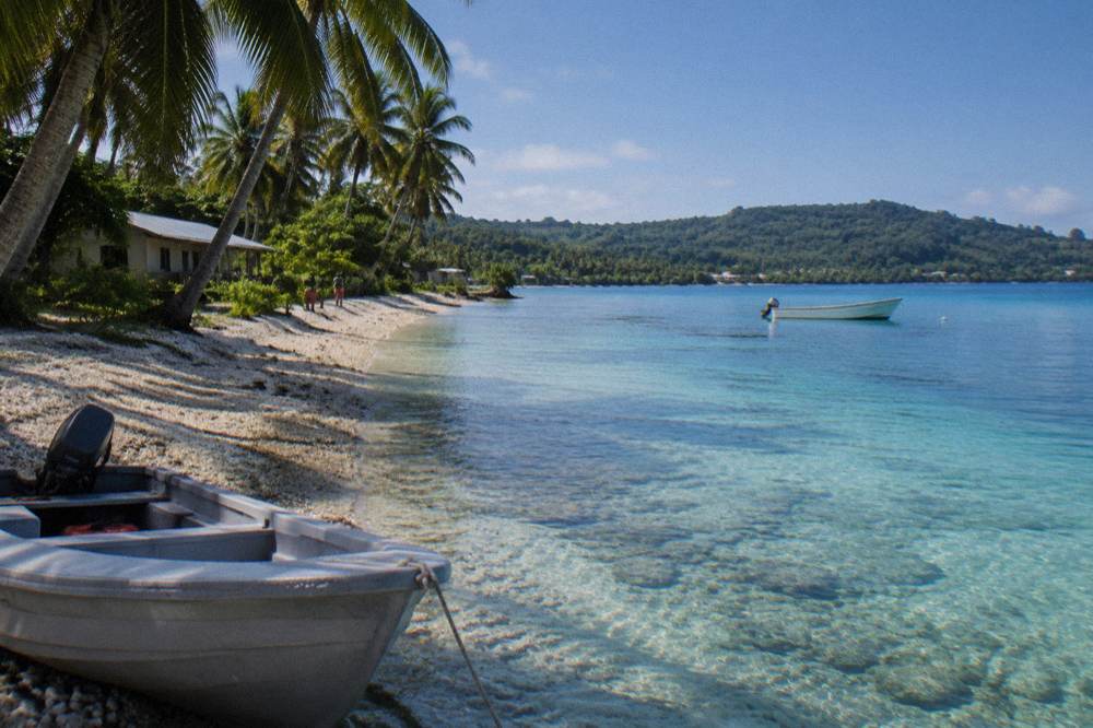 Clear morning sky over a calm turquoise bay with a small boat anchored offshore