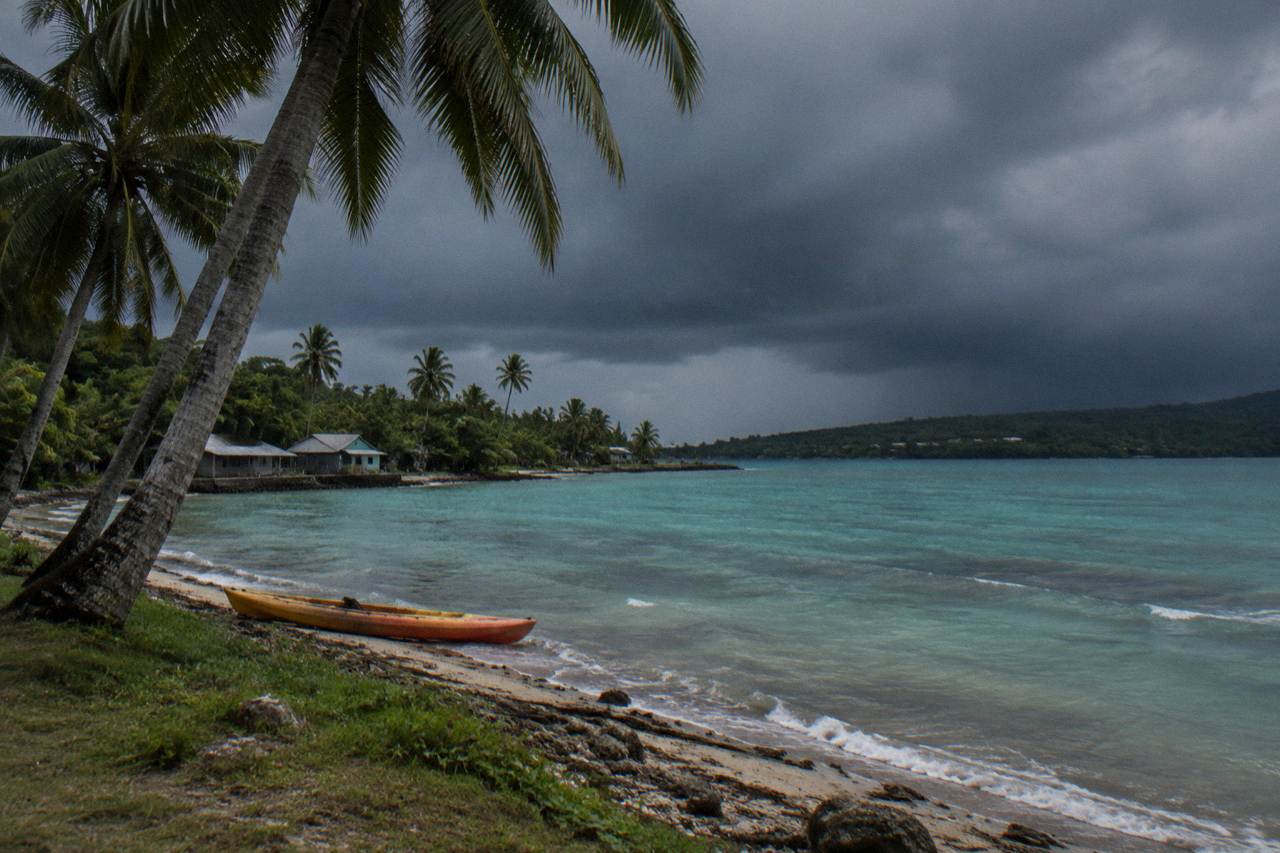 Dark storm clouds building over a calm tropical lagoon with coconut palms along the shore