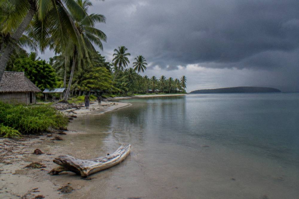 Dramatic dark storm clouds building over a calm tropical sea near a palm lined shoreline