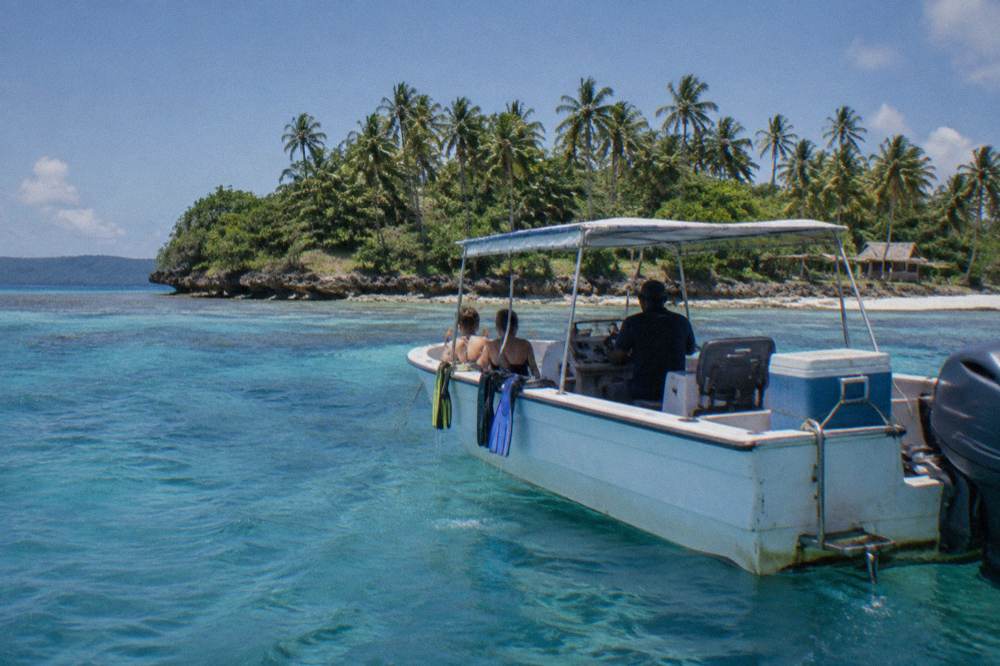 A tour boat anchored beside a reef in clear blue water with palm trees on a small island
