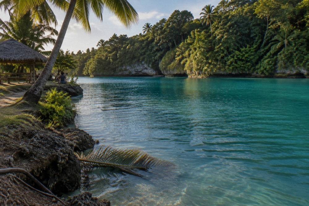 Sunlight over calm turquoise water ringed by green jungle on a clear day