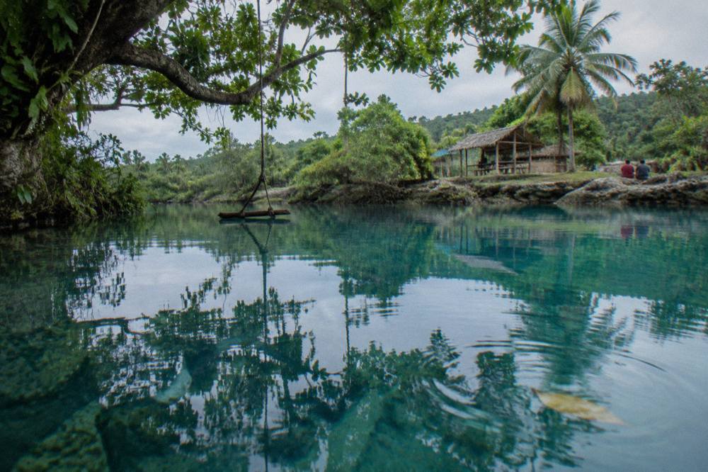 Clear blue lagoon water with overhanging trees and a rope swing above the surface