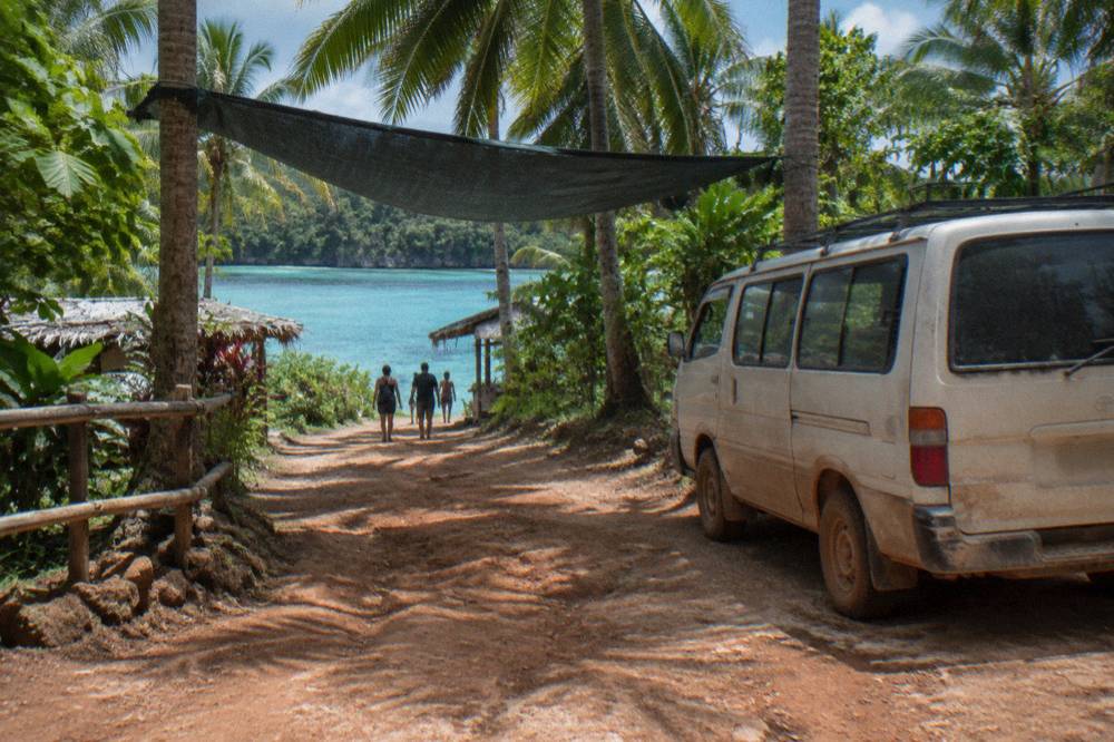 Tour van parked on a dirt road beside palm trees near a lagoon entrance