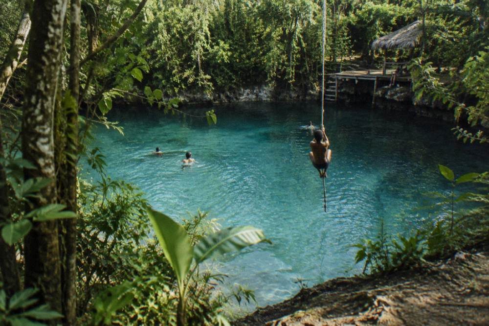 Swimmers in calm turquoise water surrounded by dense green jungle