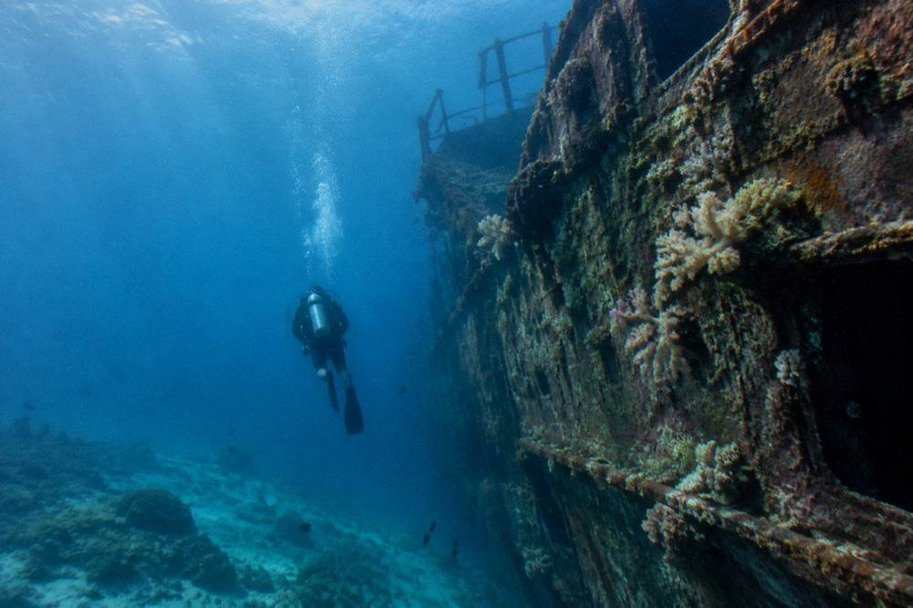 Diver descending along a sunken ship hull in blue water
