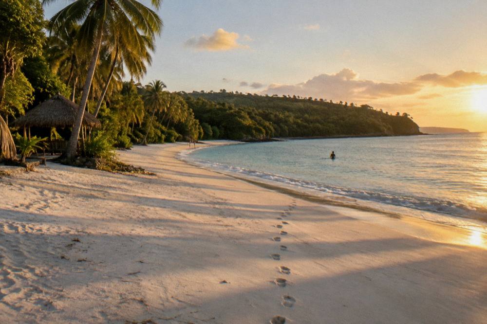 Wide empty beach at golden hour with long shadows on white sand