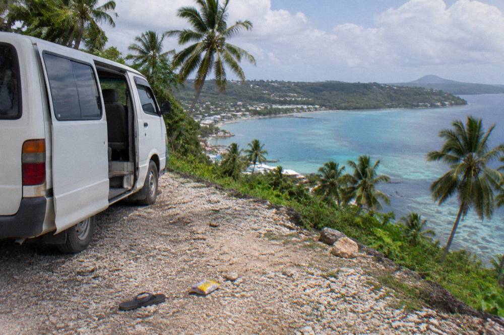 Tour van parked at a coastal lookout above a reef-fringed Efate beach