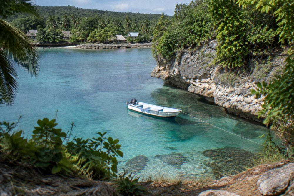Small boat anchored over clear reef water beside a wooded Vanuatu islet