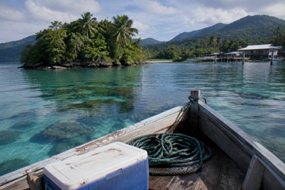 Small boat moored over shallow reef water near an island
