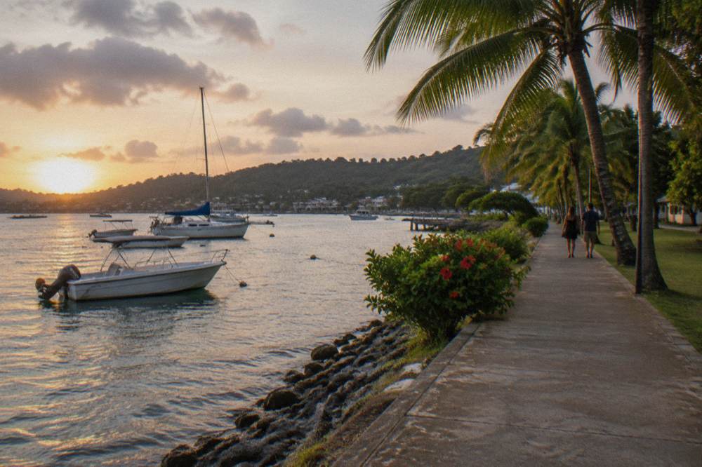 A paved seafront path beside calm harbour water with moored boats