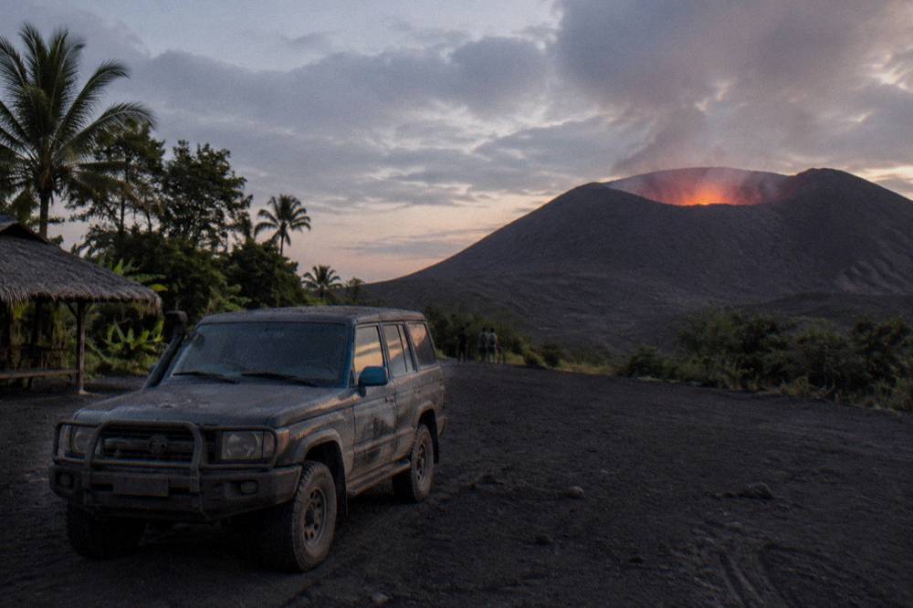 A tour vehicle parked on the ash plain below Mount Yasur at dusk