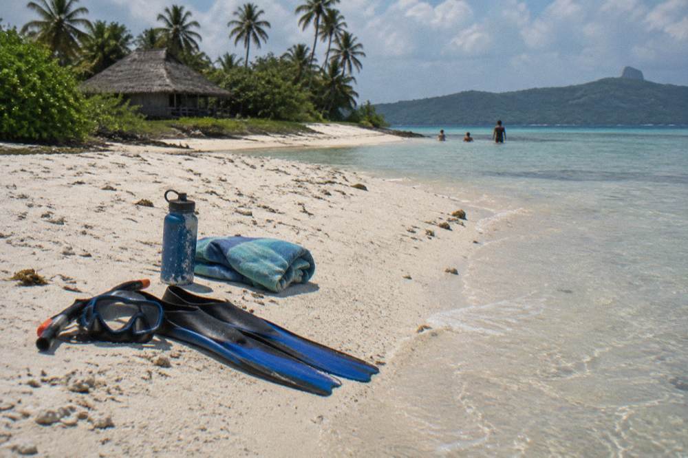 Snorkel mask and fins resting on white sand beside gentle clear water.
