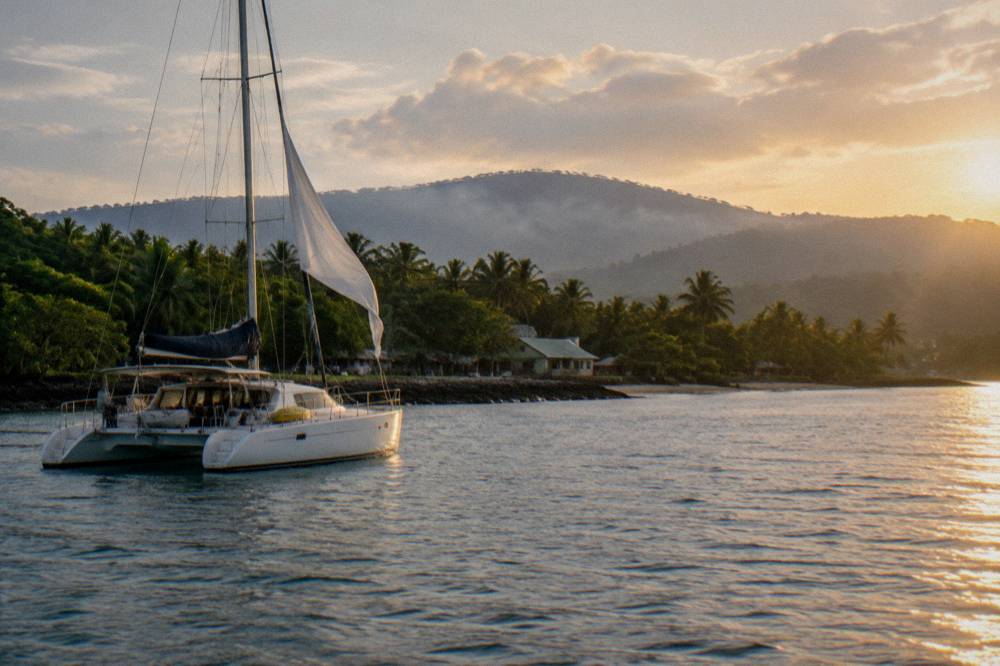 Sailing catamaran anchored near a green tropical island coastline.
