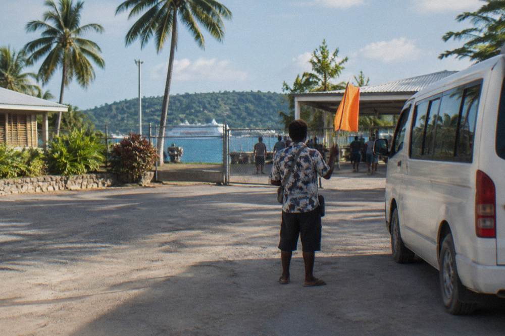 Tour guide holding a sign beside a minibus at a tropical port entrance