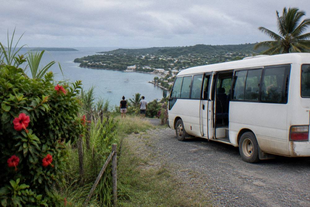 Small tour van parked on a gravel roadside beside tropical vegetation