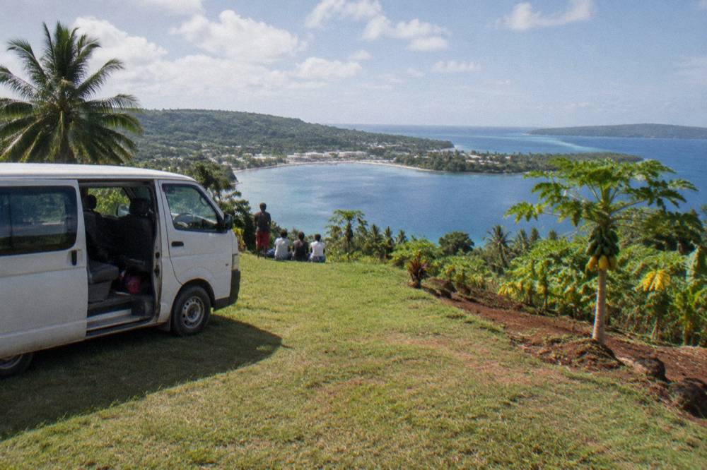 Tour van parked at a grassy lookout above a bay on the Efate ring road