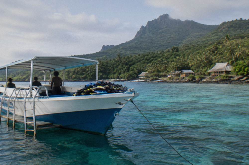 Snorkelling boat anchored over pale blue reef water beside a wooded island