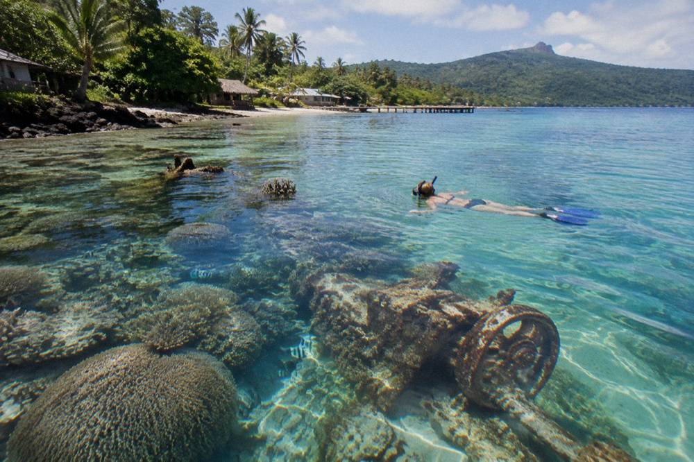 A snorkeller floating over a shallow coral reef with small fish around the coral heads
