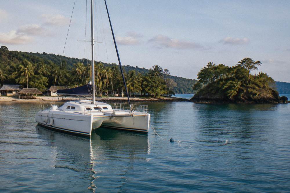 Sailing catamaran anchored near a reef island in calm blue water