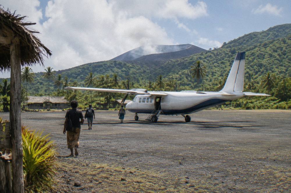 Small twin-engine aircraft parked on a tropical island airstrip with green hills in the background