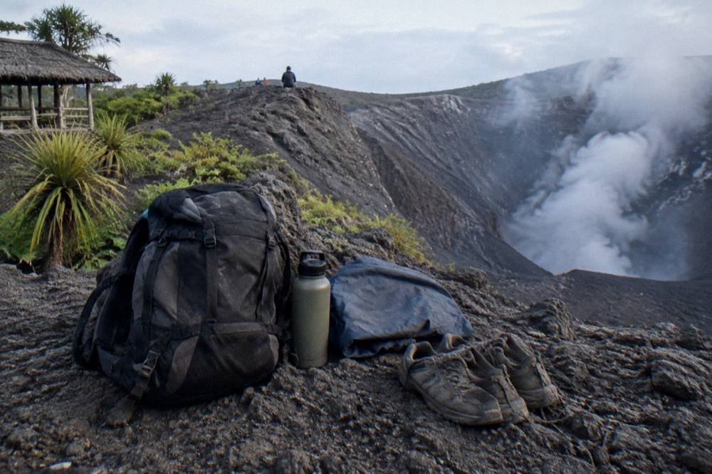 Traveller backpack with water bottle, jacket and sturdy walking shoes resting on volcanic rock