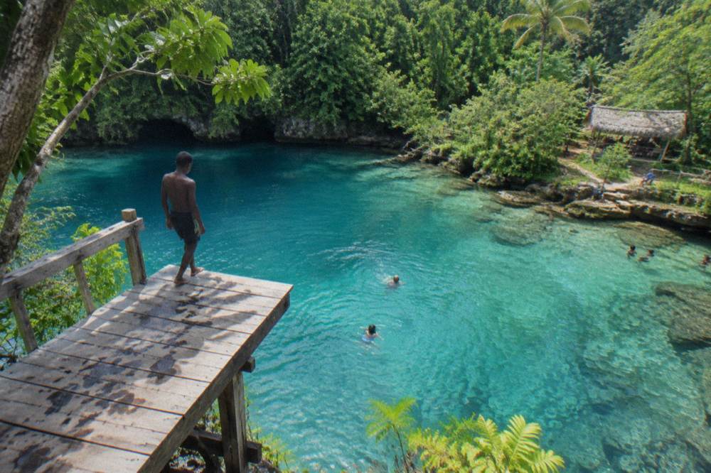 Turquoise blue lagoon surrounded by dense green jungle and a wooden jumping platform