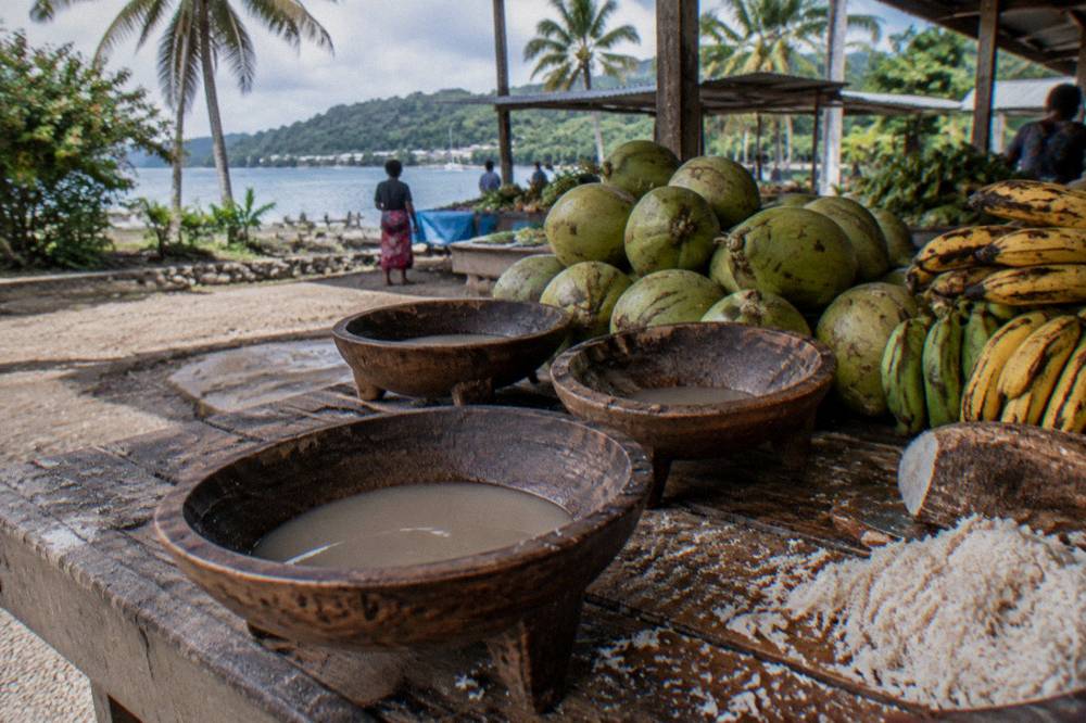 Wooden bowls of kava and fresh tropical fruit arranged on a market stall counter
