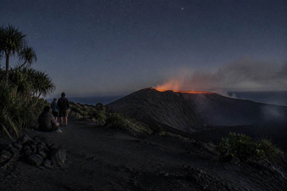 A volcanic crater rim at dusk with smoke rising from a dark ash plain below